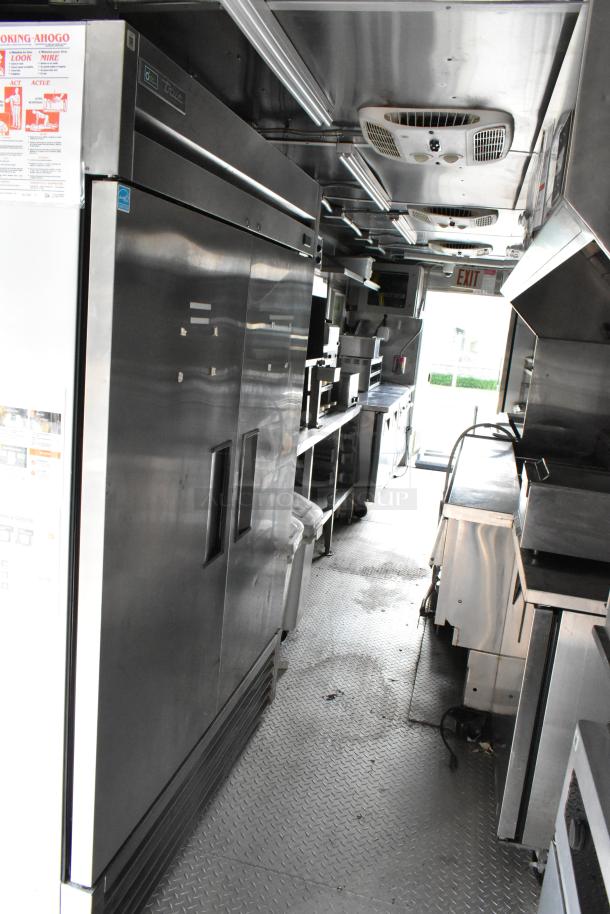 Fully equipped food trailer interior with stainless steel appliances, including a double-door refrigerator, cooking fixtures, and storage space. Ready for business.