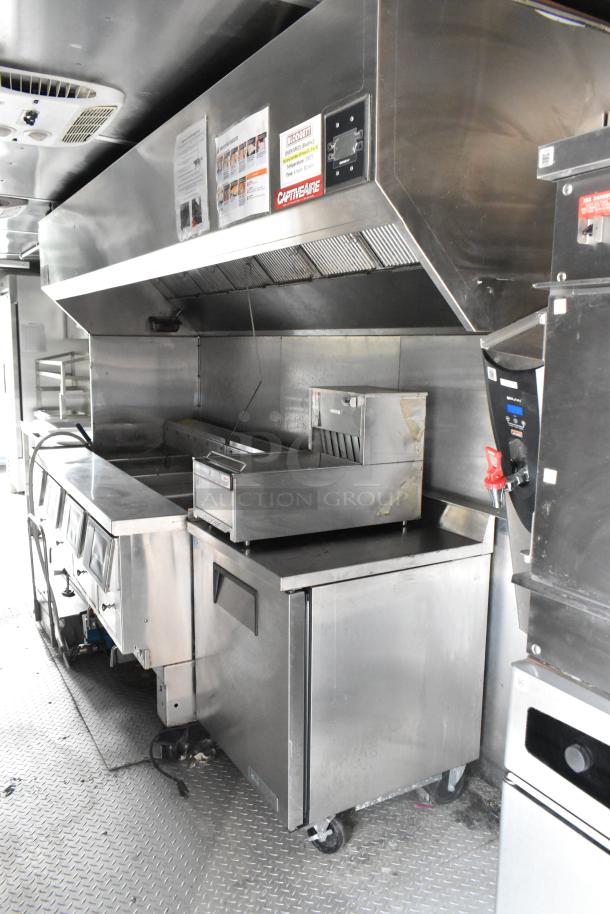 Fully equipped stainless steel food trailer interior with fryer, refrigerator, exhaust hood, and storage; ready for use.
