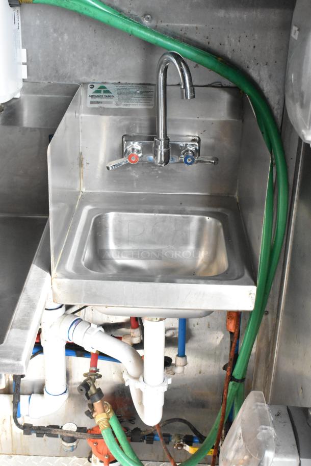 Stainless steel sink in food trailer, features dual-handle faucet. Advance Tabco label visible. Clean and well-maintained.