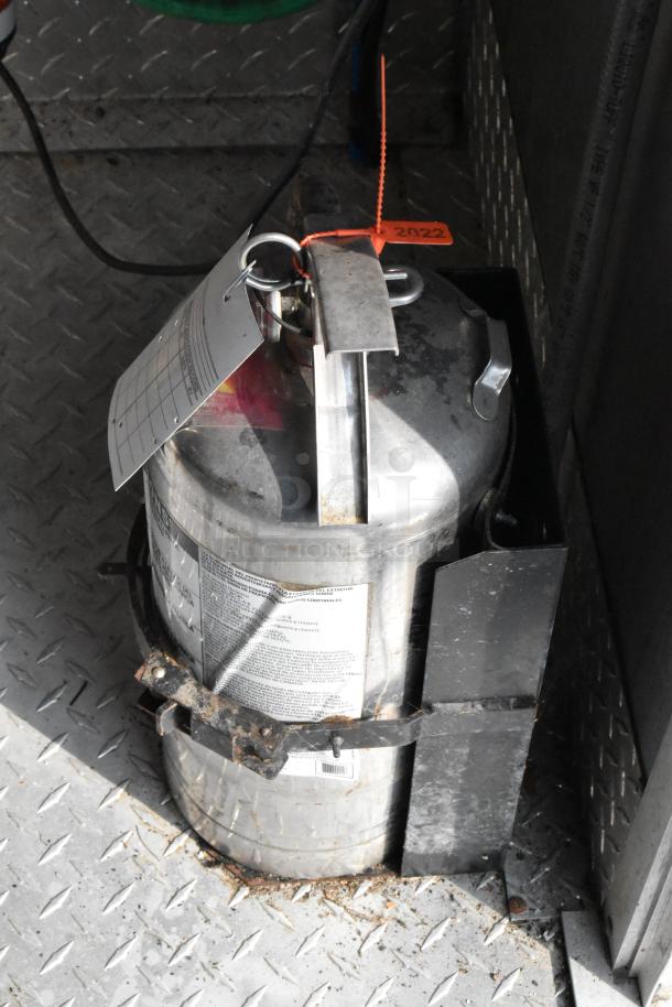 Stainless steel container in a food trailer, secured on a diamond plate floor. Tag labeled "2022" attached.