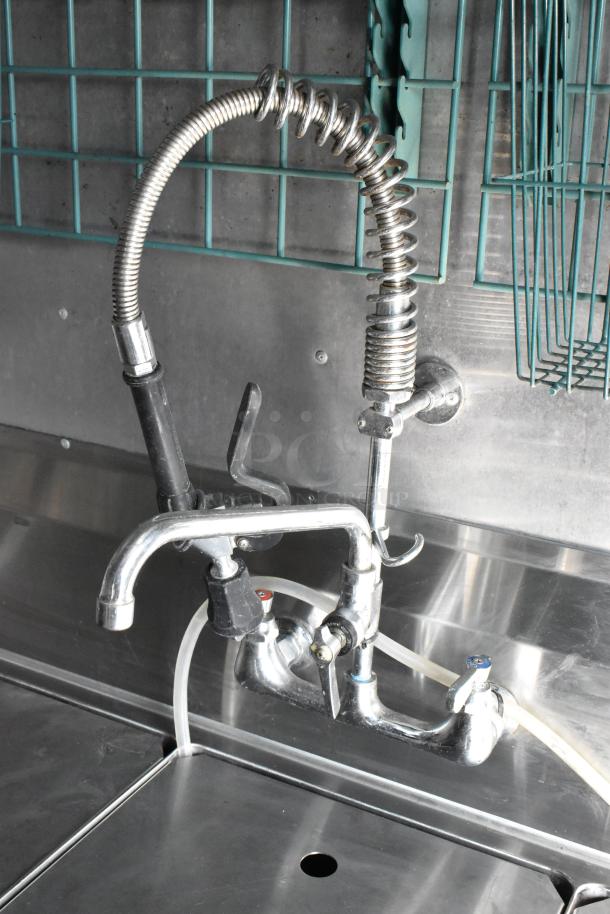 Stainless steel sink with commercial sprayer faucet in a food trailer, featuring durable fixtures and utility shelving.