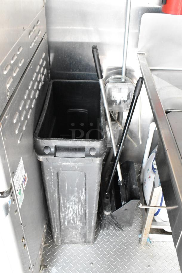 Food trailer interior with broom, dustpan, and waste bin on diamond plate flooring; appliances not visible.