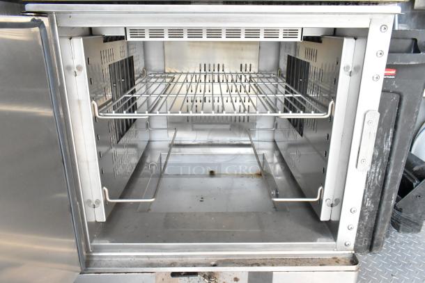 Interior view of a stainless steel food trailer oven, featuring wire shelving and a vented back panel. Clean and ready for use.