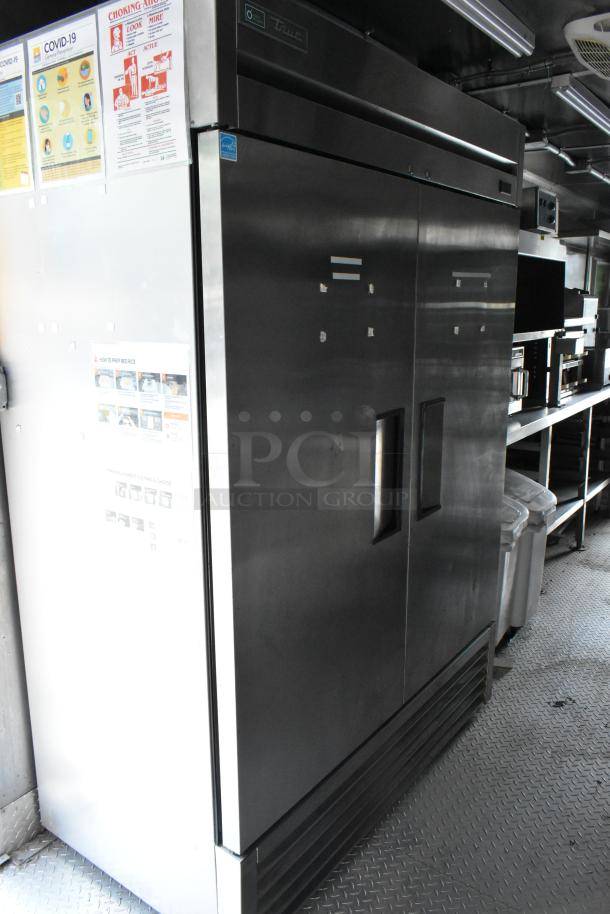 Fully equipped food trailer interior with stainless steel True refrigerator, shelving, and COVID-19 safety posters displayed.