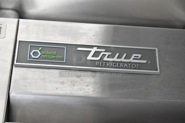 Alt text: True refrigerator with "natural refrigerant" label, stainless steel finish, in a fully outfitted food trailer.