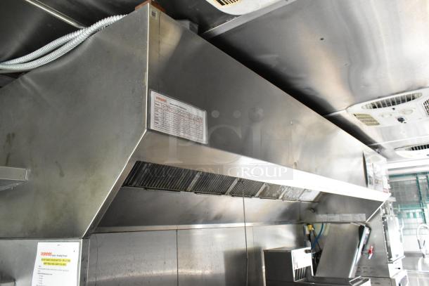 Fully outfitted food trailer kitchen with stainless steel hood, ventilation system, and instructions posted for equipment use.