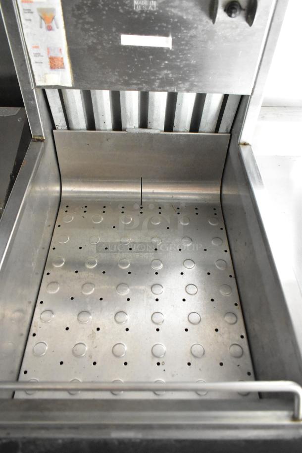 Stainless steel interior of food trailer appliance with perforated tray, labels for use, and well-maintained condition.