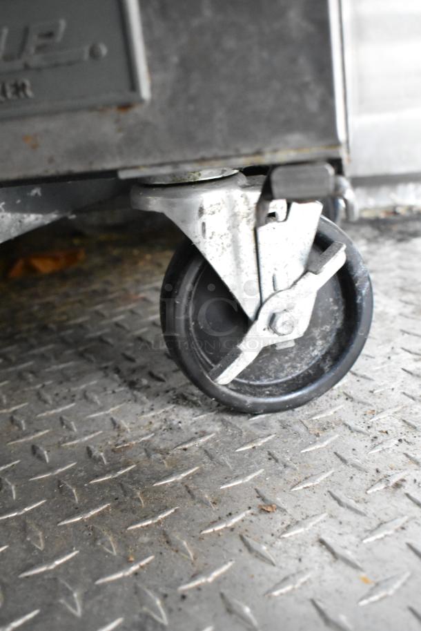 Close-up of a caster wheel attached to a food trailer on a diamond plate floor. Visible wear indicates used condition.