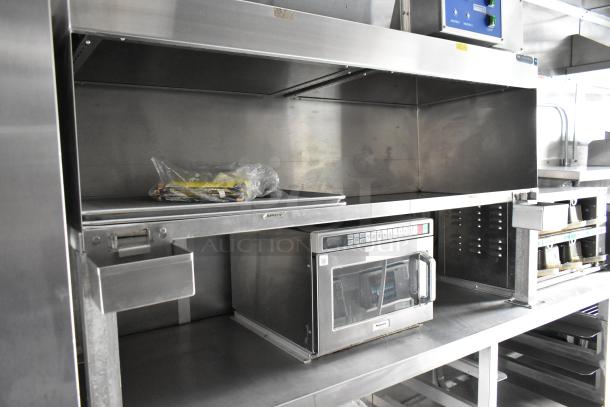 Fully equipped food trailer interior featuring a Panasonic commercial microwave, stainless steel shelving, and various fixtures.