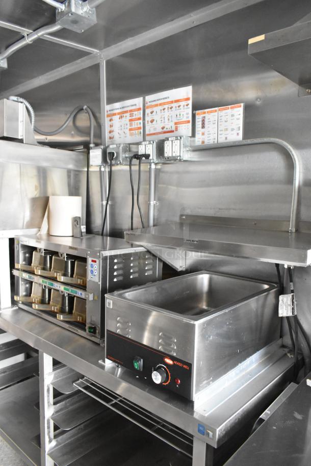 Stainless steel food trailer interior with warming oven, shelves, and wall-mounted menus. Ready for opening day.