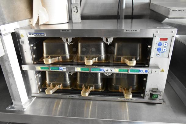 Stainless steel food warmer in a fully outfitted trailer, with labeled trays for mild, filet, spicy, and nuggets. "Prince Castle" brand.
