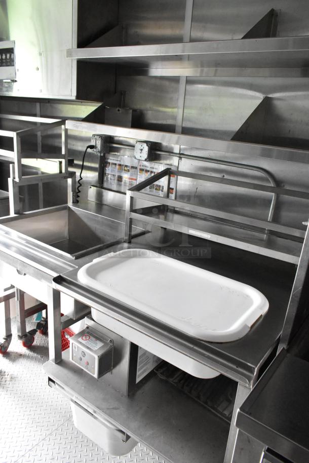 Fully outfitted food trailer interior with stainless steel prep area, sink, shelving, and appliances. Ready for use.