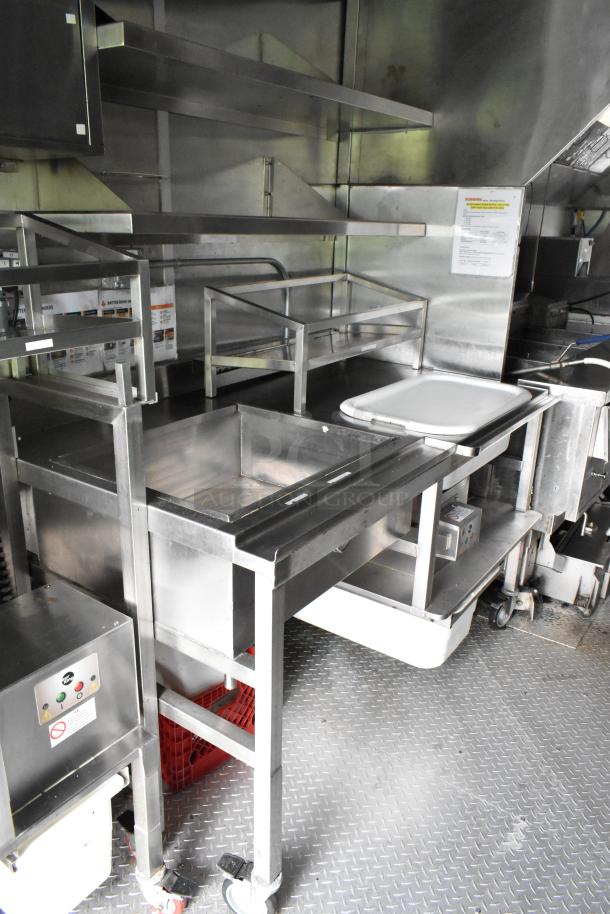 Fully equipped food trailer interior, featuring stainless steel appliances, shelving, countertops, and an industrial sink. Clean and ready for use.