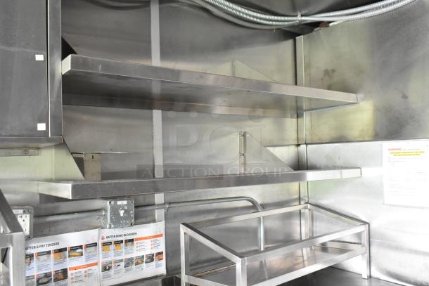 Fully outfitted food trailer interior with stainless steel shelves and fixtures, ready for use. Visible operation instructions.