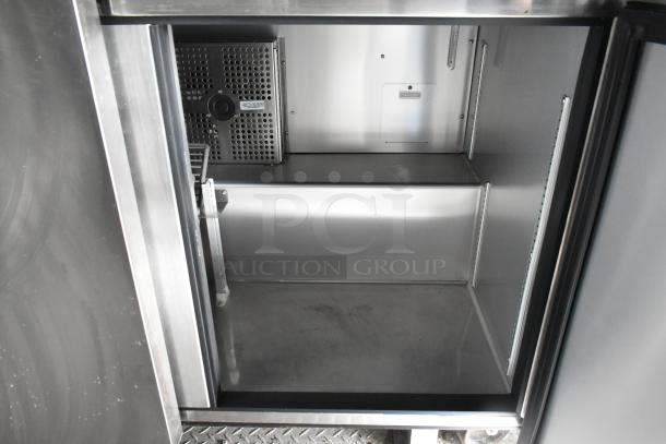 Interior view of food trailer refrigerator, stainless steel, clean, with shelving tracks and cooling fan visible.