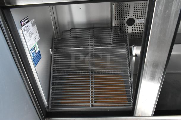 Alt text: Interior of a stainless steel food trailer refrigerator with wire shelving and a True manufacturing label.