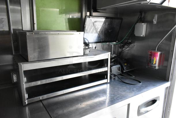 Fully outfitted food trailer interior with stainless steel fixtures, storage shelves, and a touchscreen monitor, ready for use.