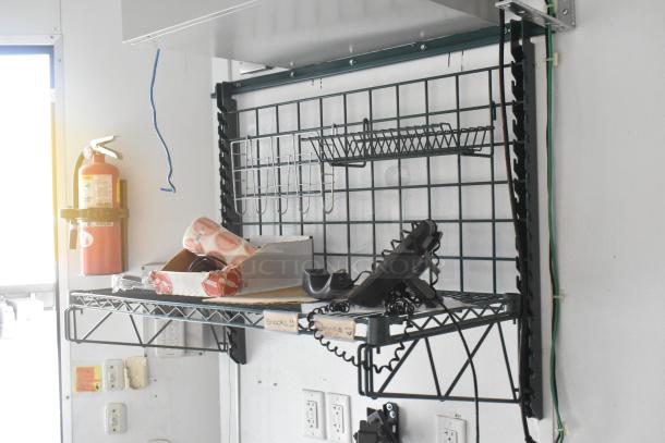 Metal rack shelf inside SDG Trailers trailer, featuring a mounted fire extinguisher, grid wall organizer, and various items.