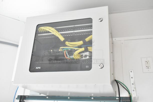 Network equipment housed in a white cabinet within an SDG trailer. Visible APC branding, yellow cabling, and secured with screws.
