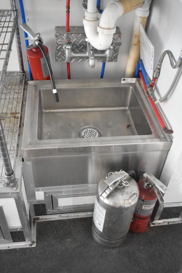Stainless steel sink with faucet and drain, mounted in SDG trailer. Includes fire extinguisher. Visible plumbing and storage rack.