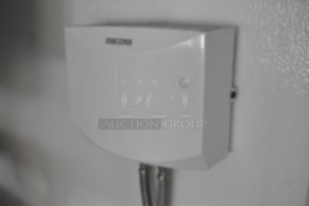 White wall-mounted appliance, rectangular shape, connection cables below. Label reads "Bell Topca."