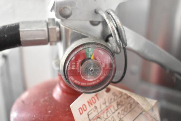 Close-up of a fire extinguisher gauge showing pressure in the green range, attached to an SDG Trailer appliance. Visible tag with warnings.