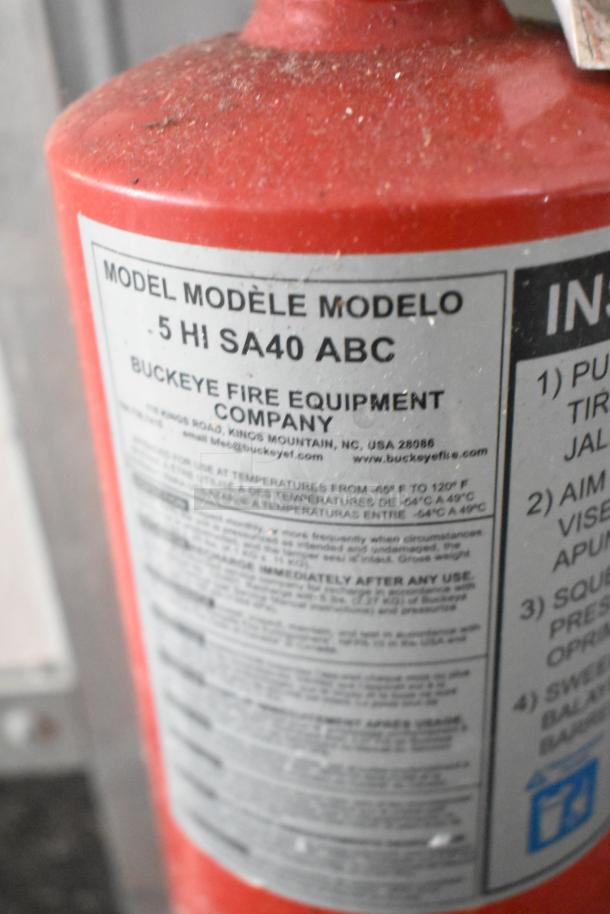 Red fire extinguisher by Buckeye Fire Equipment Company, Model 5 HI SA40 ABC. Visible label with safety instructions. Slightly dusty.