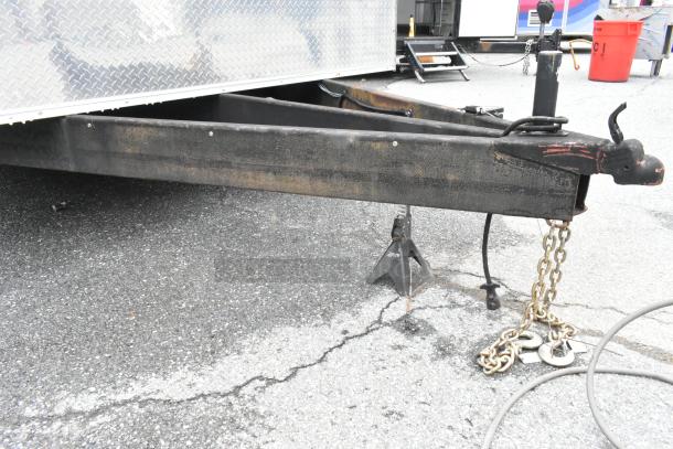 Food trailer hitch area with chains and jack stands on asphalt, featuring a diamond-patterned metallic exterior.