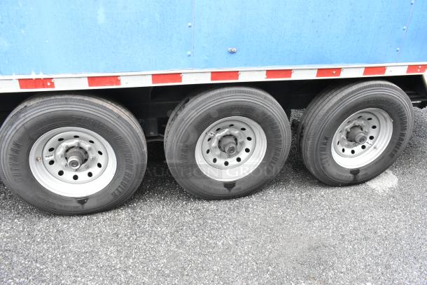 Triple axle food trailer with white rims and Freedom Hauler tires, showcasing side detail of the trailer's blue exterior.
