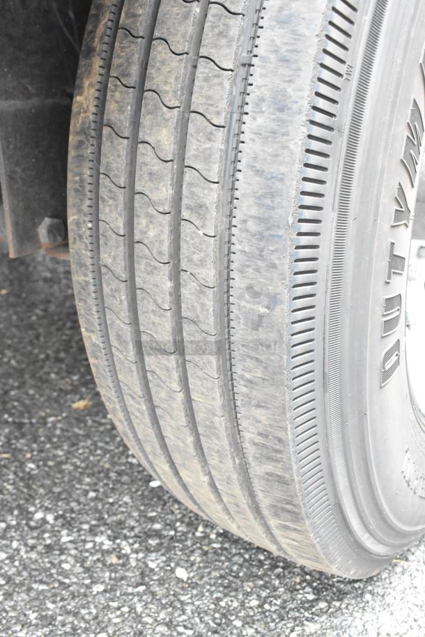 Close-up of a trailer tire in good condition, showing tread pattern and sidewall markings on asphalt.