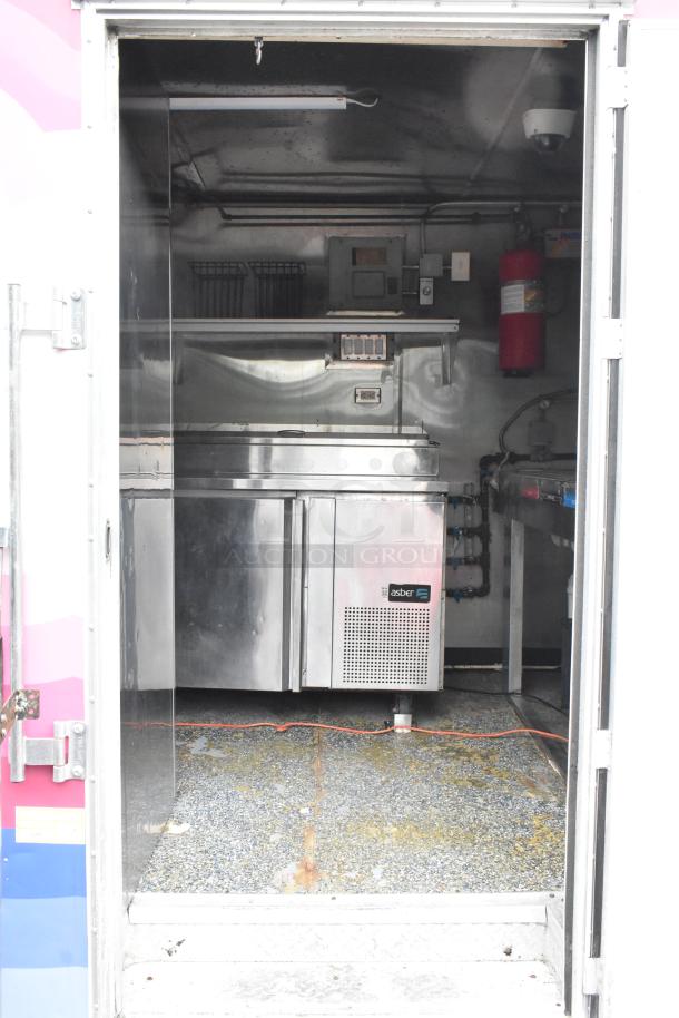 Fully equipped food trailer interior with stainless steel appliances, Asber refrigeration, fire extinguisher, and utility fixtures.