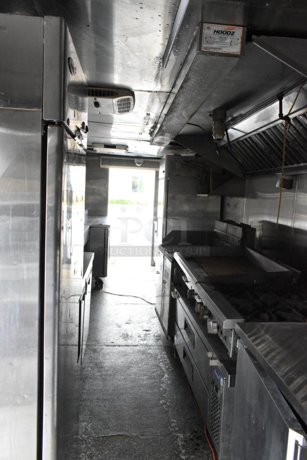 Fully outfitted food trailer interior with professional kitchen appliances, stainless steel surfaces, and overhead exhaust system.
