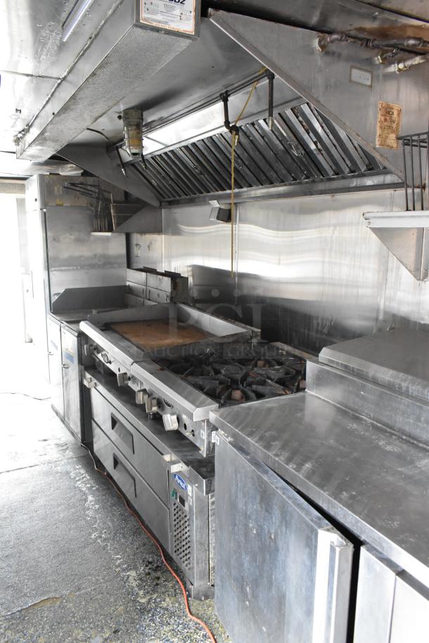 Fully equipped food trailer interior with stainless steel appliances, grill, gas burners, ventilation hood, and storage areas.
