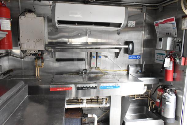 Fully equipped food trailer interior with stainless steel counters, air conditioning, fire extinguishers, and labeled water lines.