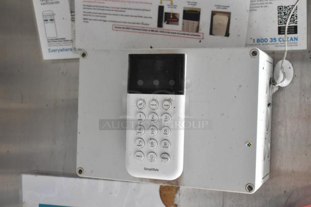 Security keypad mounted on a white control box inside a food trailer. Simplisafe branding visible.