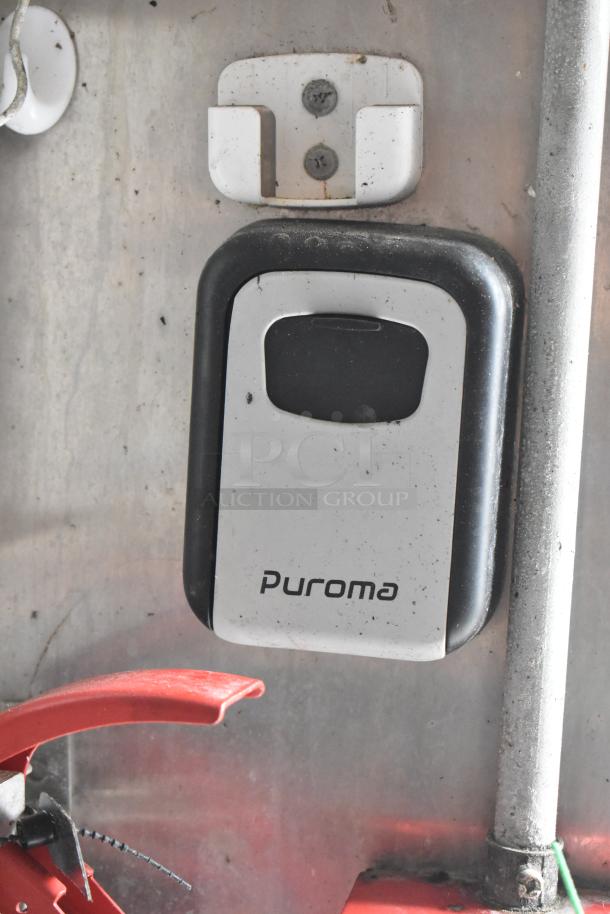 Puroma lockbox mounted on food trailer wall, showing slight wear, securely stored beneath shelf.