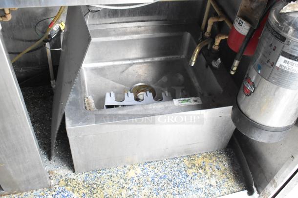 Stainless steel sink in food trailer with Regency NSF label, showing plumbing and fire extinguisher nearby. Clean condition.