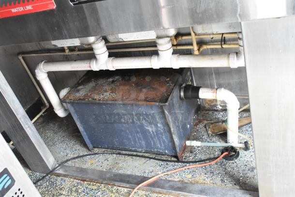 Food trailer plumbing system with visible pipes and connections. Slight rust on a metal casing. Essential setup for operation.