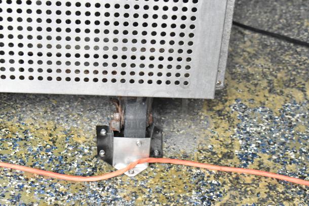 Close-up of food trailer wheel with metal casing and perforated panel. Orange cable visible on speckled floor.