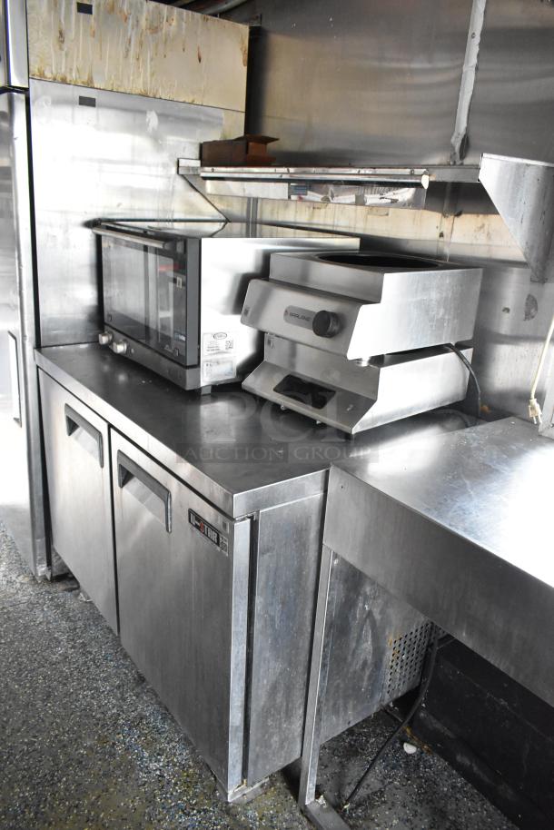 Stainless steel food trailer interior with Garland appliances, under-counter fridge, and shelving. Clean, ready for use.