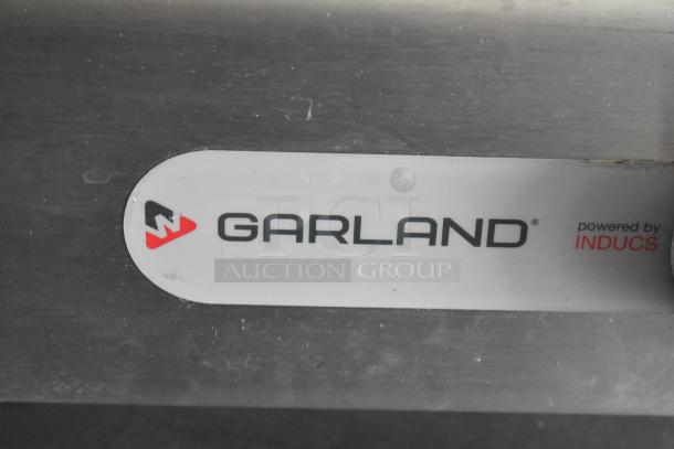 Label showing "Garland, powered by Inducs" on a stainless steel surface, indicating appliance brand in a food trailer.