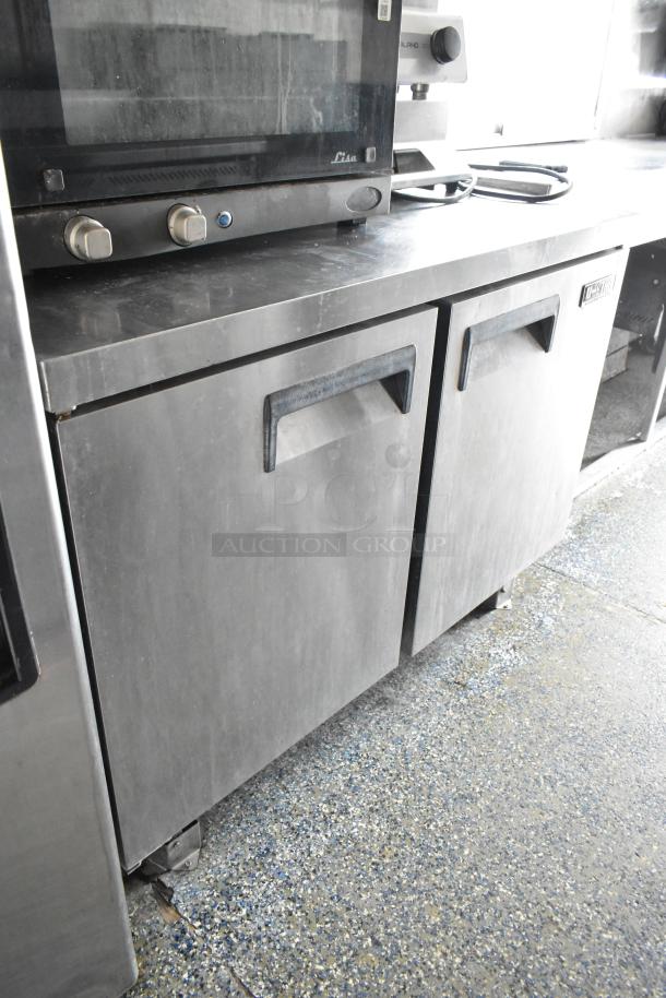 Stainless steel food trailer interior with a two-door refrigerator beneath a countertop, showcasing commercial appliance setup.
