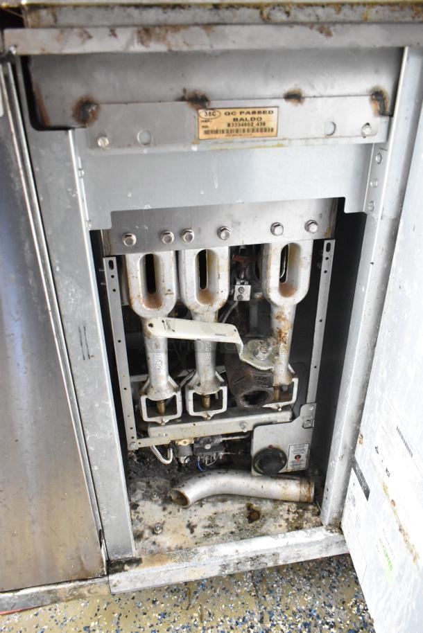 Interior view of food trailer appliance showing metal burners and a QC passed label. Signs of rust and wear throughout.