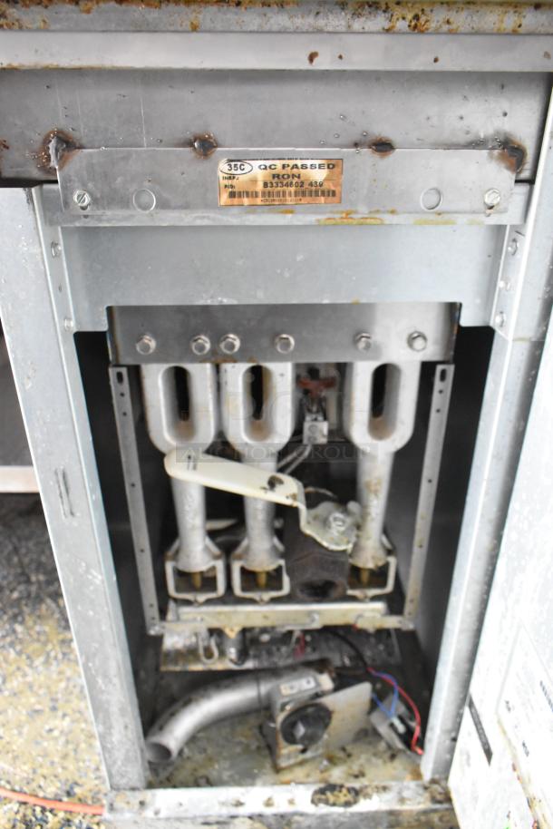 Inner components of a food trailer appliance, showing metallic fixtures, pipes, and rust. Quality control tag visible.