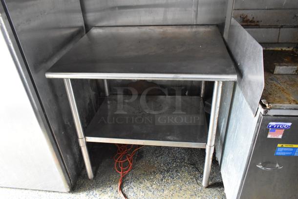 Stainless steel prep table in food trailer, two-tier design, slight wear, adjacent to Pitco appliance, ready to use.