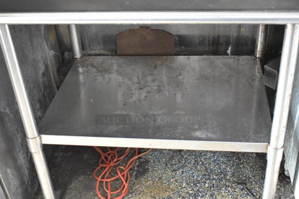 Interior shelf of a metal food trailer showing storage area with metal poles and slight rust. Orange cord lies below.