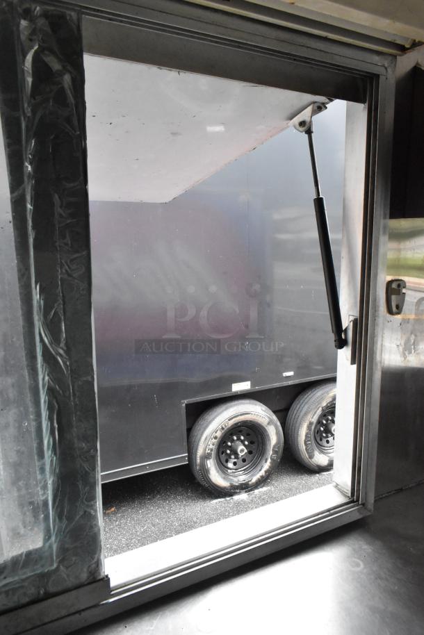 Food trailer viewed through a service window, showing dual wheels and black exterior; ready for business setup.