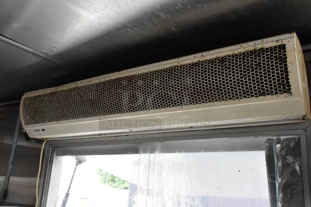 Air curtain inside a food trailer, used condition, mounted above a window. Visible wear and dirt on the grille.