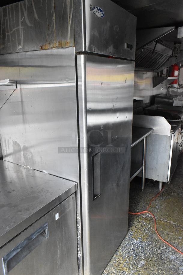 Stainless steel refrigerator in a commercial food trailer, features industrial design and visible wear.
