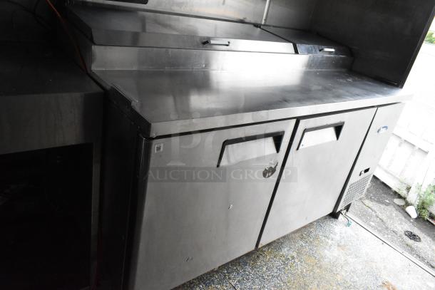 Stainless steel food trailer counter with double storage doors, handles, and worn markings, ready for use.